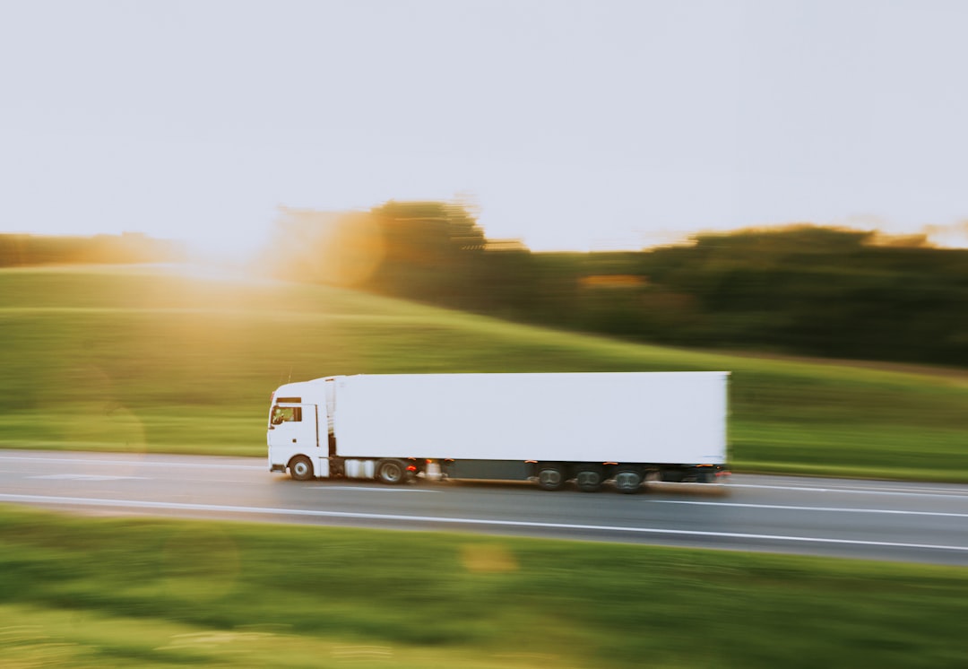 A large, white semi truck, traveling along a road at high speed.