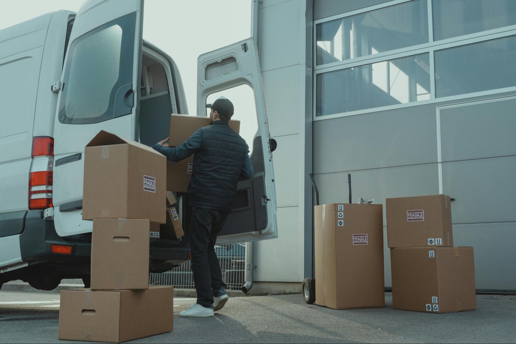 A person loading cardboard boxes into the back of a white van.