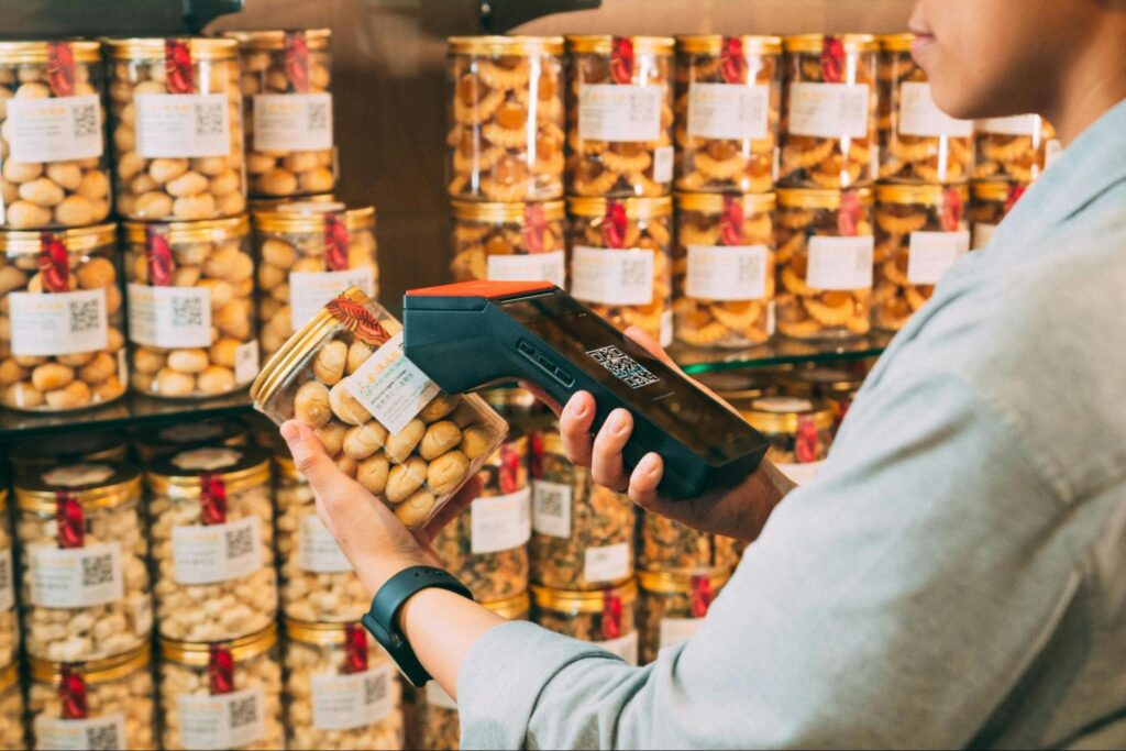 A person scanning a QR code on a small, cylindrical package of perishables.