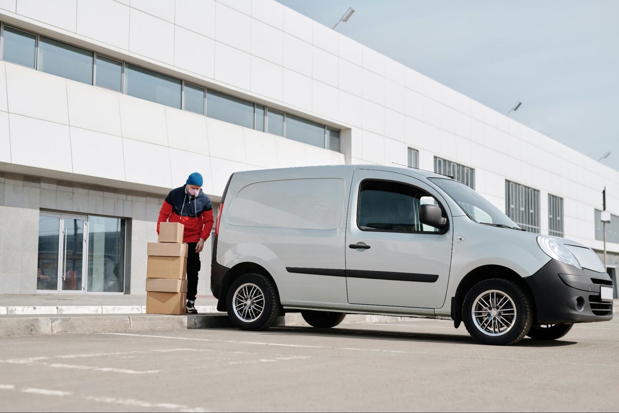 A person unloading cardboard boxes from the trunk of a small, silver van.